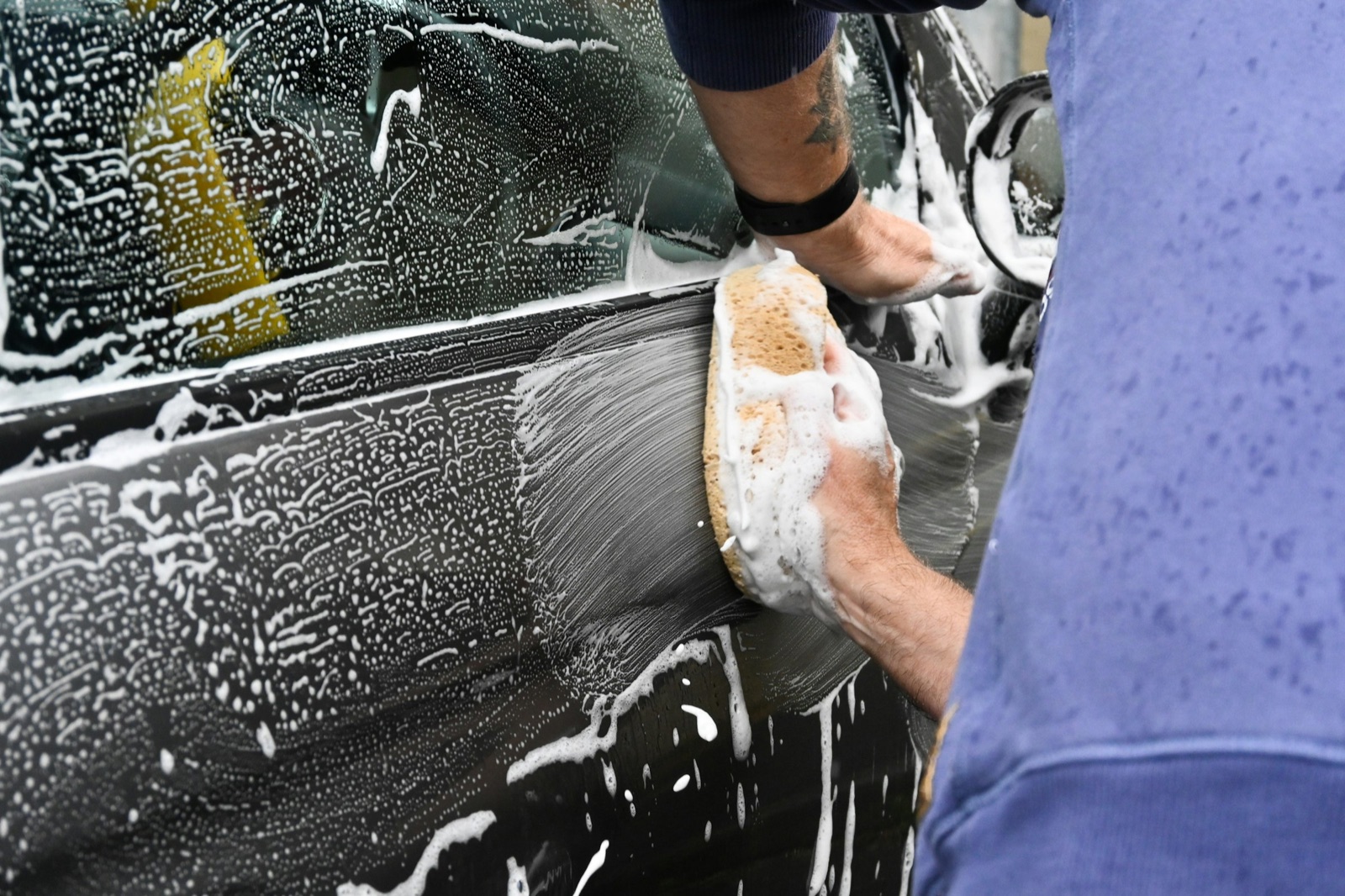 A car door being hand washed with a soapy sponge